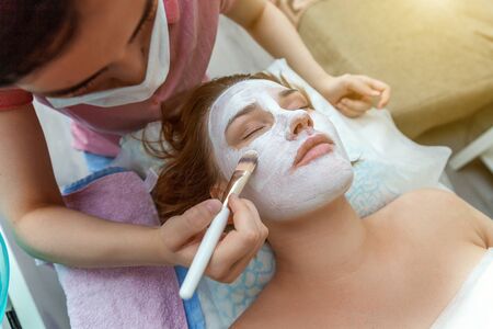 Close-up of young beauty brunette woman getting face treatment with white nourishing creme in spa salon. Face massage. Spa skin and body care. Skincare cleansing cosmetic spa relax conceptの写真素材
