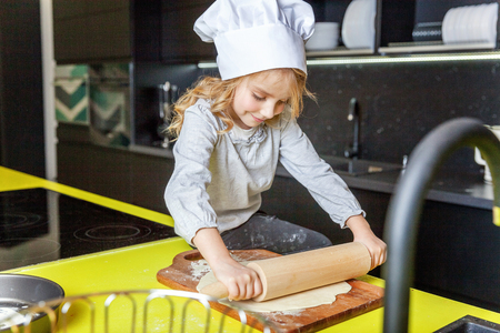 Little girl with chef hat, rolling pin preparing dough, bake homemade holiday apple pie in kitchen. Kid cooking healthy food at home and having fun. Childhood, household, teamwork helping conceptの写真素材