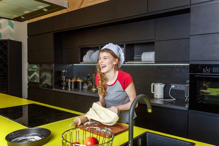 Teenage girl with chef hat, rolling pin preparing dough, bake homemade holiday apple pie in kitchen. Young woman cooking healthy food at home and having fun. Food, healthy eating, household conceptの写真素材