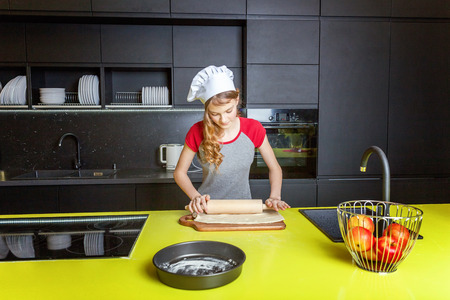 Teenage girl with chef hat, rolling pin preparing dough, bake homemade holiday apple pie in kitchen. Young woman cooking healthy food at home and having fun. Food, healthy eating, household conceptの写真素材