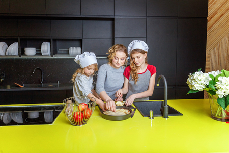 Happy family in kitchen. Mother and two children preparing dough, bake apple pie. Mom and daughters cooking healthy food at home and having fun. Household, teamwork helping, maternity conceptの写真素材