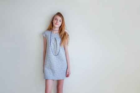 Happy teenage girl smiling. Closeup portrait young happy positive woman in grey dress at home in bright room against white wall. European woman. Positive human emotion facial expression body languageの写真素材