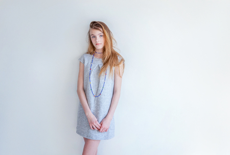 Happy teenage girl smiling. Closeup portrait young happy positive woman in grey dress at home in bright room against white wall. European woman. Positive human emotion facial expression body languageの写真素材