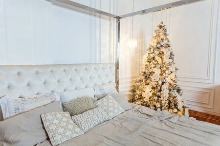 Classic Christmas decorated interior room New year tree. Christmas tree with gold decorations. Modern white classical style interior design apartment bedroom with bed. Christmas eve at homeの写真素材