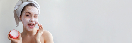 Beauty portrait of woman in towel on head with white nourishing mask or creme on face, white background isolated. Skincare cleansing eco organic cosmetic spa relax concept Bannerの写真素材