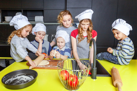 Happy family in kitchen. Mother and five children preparing dough, bake apple pie. Mom, daughters and sons cooking healthy food at home and having fun. Household, teamwork helping, maternity conceptの写真素材