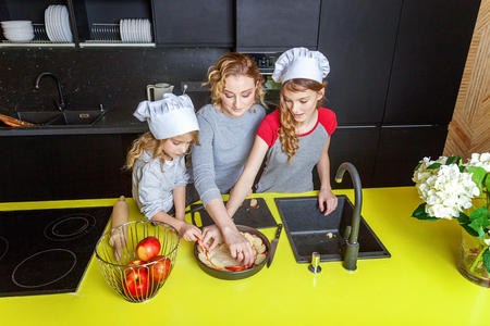 Happy family in kitchen. Mother and two children preparing dough, bake apple pie. Mom and daughters cooking healthy food at home and having fun. Household, teamwork helping, maternity conceptの写真素材