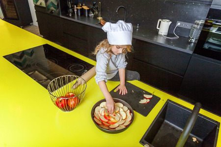 Little girl with chef hat preparing bake homemade holiday apple pie in kitchen. Kid cooking healthy food at home and having fun. Childhood, household, teamwork helping conceptの写真素材
