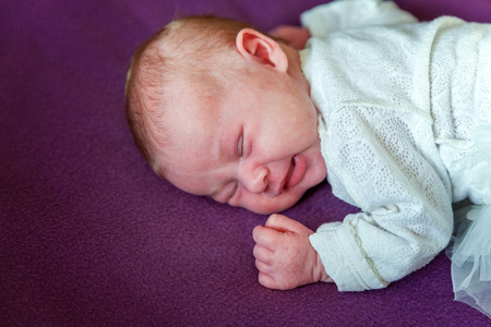 Soft portrait of peaceful sweet newborn infant baby lying on bed while sleeping in purple blanket background. Sweet dream, good night. Maternity family childhood innocence care conceptの写真素材