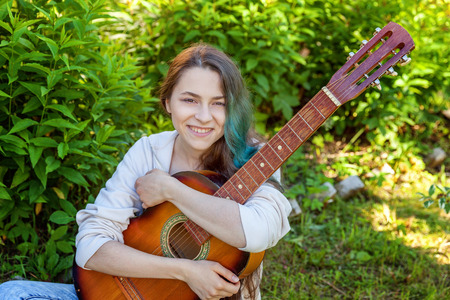 Young hipster woman sitting in grass and playing guitar on park or garden background. Teen girl learning to play song and writing music. Hobby, lifestyle, relax, Instrument, leisure, education conceptの写真素材