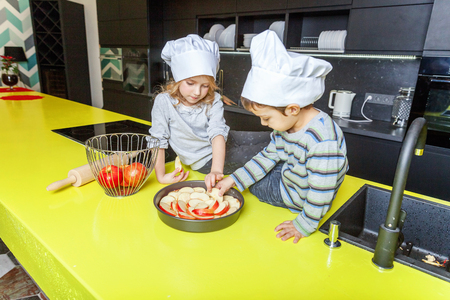 Little kids girl and boy with chef hat preparing bake homemade apple pie in kitchen. Brother and sister cooking healthy food at home and having fun. Childhood, household, teamwork helping conceptの写真素材