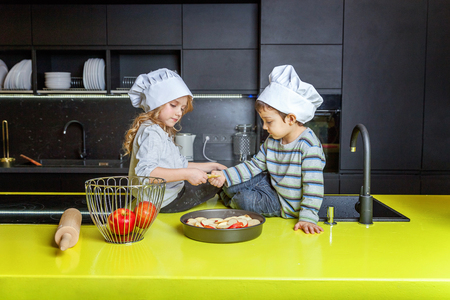 Little kids girl and boy with chef hat preparing bake homemade apple pie in kitchen. Brother and sister cooking healthy food at home and having fun. Childhood, household, teamwork helping conceptの写真素材