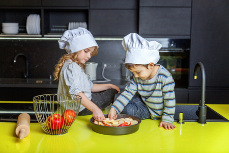 Little kids girl and boy with chef hat preparing bake homemade apple pie in kitchen. Brother and sister cooking healthy food at home and having fun. Childhood, household, teamwork helping conceptの写真素材