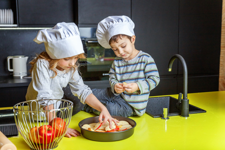 Little kids girl and boy with chef hat preparing bake homemade apple pie in kitchen. Brother and sister cooking healthy food at home and having fun. Childhood, household, teamwork helping conceptの写真素材