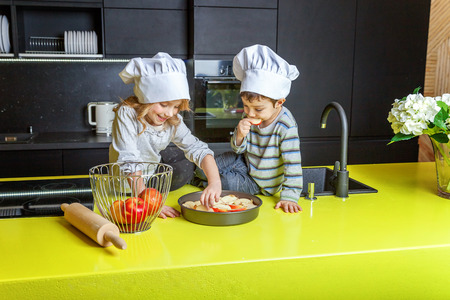 Little kids girl and boy with chef hat preparing bake homemade apple pie in kitchen. Brother and sister cooking healthy food at home and having fun. Childhood, household, teamwork helping conceptの写真素材