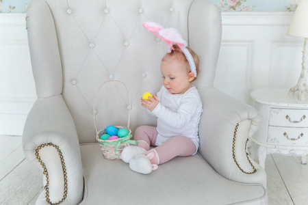 Little child girl wearing bunny ears on Easter day. Girl holding basket with painted eggs at home decoration, having fun on Easter egg hunt. Happy Easter holiday celebration spring conceptの写真素材