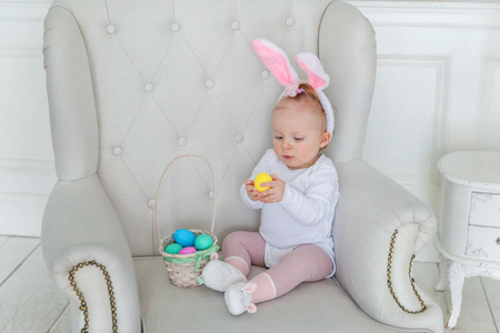 Little child girl wearing bunny ears on Easter day. Girl holding basket with painted eggs at home decoration, having fun on Easter egg hunt. Happy Easter holiday celebration spring conceptの写真素材