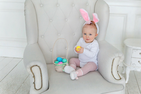 Little child girl wearing bunny ears on Easter day. Girl holding basket with painted eggs at home decoration, having fun on Easter egg hunt. Happy Easter holiday celebration spring conceptの写真素材