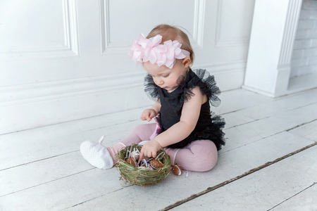 Little child girl wearing spring wreath on Easter day. Girl holding basket with painted eggs at home decoration, having fun on Easter egg hunt. Happy Easter holiday celebration conceptの写真素材