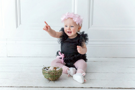Little child girl wearing spring wreath on Easter day. Girl holding basket with painted eggs at home decoration, having fun on Easter egg hunt. Happy Easter holiday celebration conceptの写真素材