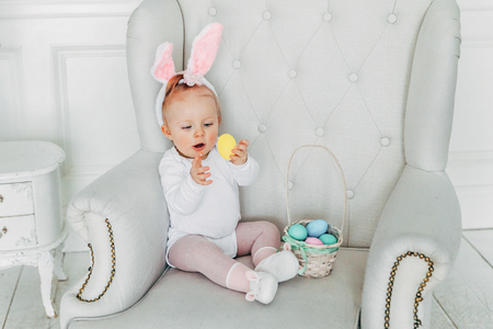 Little child girl wearing bunny ears on Easter day. Girl holding basket with painted eggs at home decoration, having fun on Easter egg hunt. Happy Easter holiday celebration spring conceptの写真素材