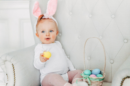 Little child girl wearing bunny ears on Easter day. Girl holding basket with painted eggs at home decoration, having fun on Easter egg hunt. Happy Easter holiday celebration spring conceptの写真素材