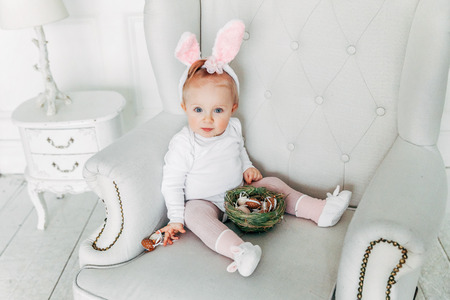 Little child girl wearing bunny ears on Easter day. Girl holding basket with painted eggs at home decoration, having fun on Easter egg hunt. Happy Easter holiday celebration spring conceptの写真素材