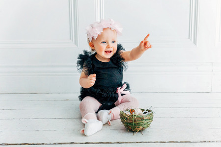 Little child girl wearing bunny ears on Easter day. Girl holding basket with painted eggs sitting on floor at home, having fun on Easter egg hunt. Happy Easter holiday celebration spring conceptの写真素材