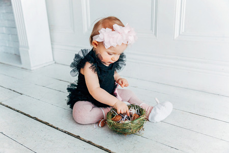 Little child girl wearing bunny ears on Easter day. Girl holding basket with painted eggs sitting on floor at home, having fun on Easter egg hunt. Happy Easter holiday celebration spring conceptの写真素材