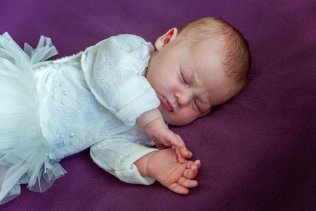 Soft portrait of peaceful sweet newborn infant baby lying on bed while sleeping in purple blanket background. Sweet dream, good night. Maternity family childhood innocence care conceptの写真素材