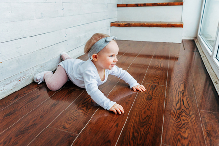Little crawling baby girl one year old siting on floor in bright light living room near window smiling and laughing. Happy toddler kid playing at home. Childhood conceptの写真素材