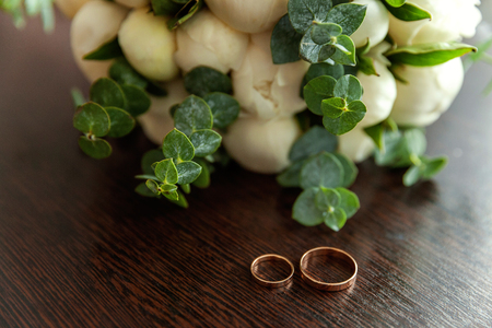 Beautiful wedding rings lie on wooden surface against background of bouquet of flowers. Declaration of love, spring. Wedding card, Valentine's Day greeting. Wedding rings. Wedding day detailsの写真素材