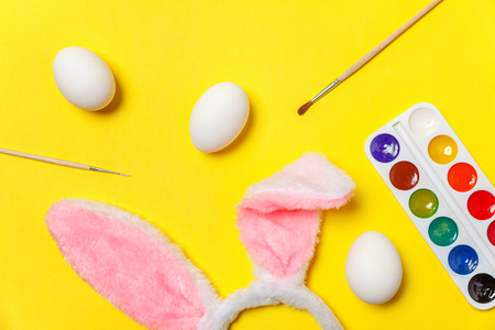 Happy Easter concept. Preparation for holiday. Decorative eggs colorful paints and bunny ears furry costume toy isolated on trendy yellow background. Simple minimalism flat lay top view copy spaceの写真素材