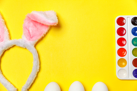 Happy Easter concept. Preparation for holiday. Decorative eggs colorful paints and bunny ears furry costume toy isolated on trendy yellow background. Simple minimalism flat lay top view copy spaceの写真素材