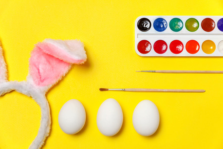 Happy Easter concept. Preparation for holiday. Decorative eggs colorful paints and bunny ears furry costume toy isolated on trendy yellow background. Simple minimalism flat lay top view copy spaceの写真素材