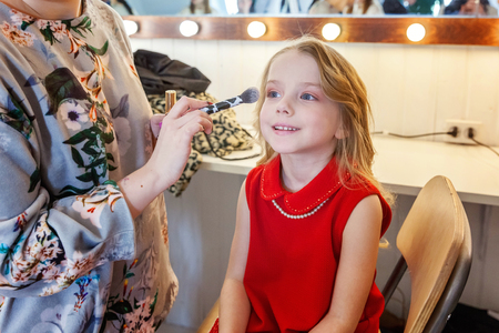 Hand of makeup master applying eyeshadow for little pretty girl model. Professional make up applying by artist. Make-up detail in process. Fashon kid beauty salon photosession conceptの写真素材