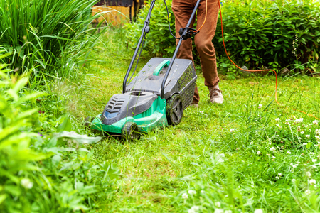 Man cutting green grass with lawn mower in backyard. Gardening country lifestyle background....
