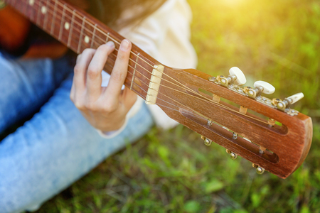 Closeup of woman hands playing acoustic guitar on park or garden background. Teen girl learning to play song and writing music. Hobby, lifestyle, relax, Instrument, leisure, education conceptの写真素材