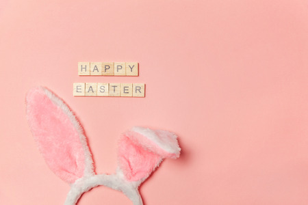 Happy Easter concept. Preparation for holiday. Inscription HAPPY EASTER letters decorative bunny ears isolated on trendy pastel pink background. Simple minimalism flat lay top view copy spaceの写真素材