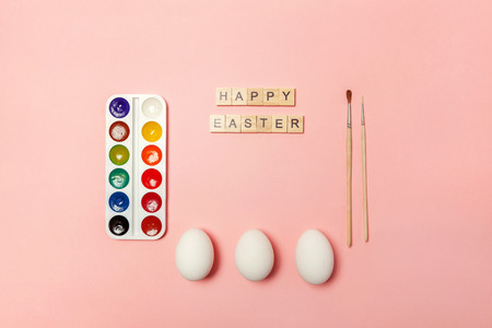 Happy Easter concept. Preparation for holiday. Inscription HAPPY EASTER letters eggs colorful paints isolated on trendy pastel pink background. Simple minimalism flat lay top view copy spaceの写真素材