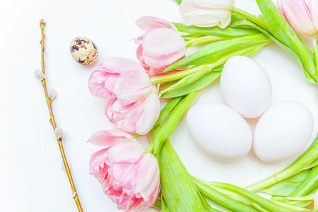 Spring greeting card. Easter eggs in nest and pink fresh tulip flowers bouquet on rustic white wooden background. Easter concept. Flat lay top view copy space. Spring flowers tulipsの写真素材