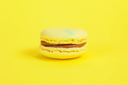 Sweet almond colorful yellow macaron or macaroon dessert cake isolated on trendy yellow modern fashion background. French sweet cookie. Minimal food bakery concept. Copy spaceの写真素材