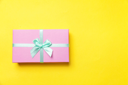 Christmas New Year birthday valentine celebration present romantic concept. Gift box wrapped pink paper isolated on yellow colourful trendy modern fashion background. Flat lay top view copy spaceの写真素材
