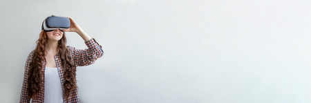 Technology, simulation, hi-tech, videogame concept. Young woman wearing using virtual reality VR glasses helmet headset on white background. Smartphone using with virtual reality goggles. Bannerの写真素材