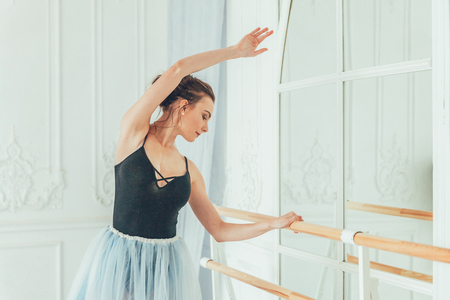 Young classical ballet dancer woman in dance class. Beautiful graceful ballerina practice ballet positions in blue tutu skirt near large mirror in white light hallの写真素材