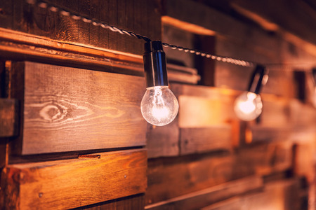 Modern dark classical style interior design apartment with retro lamps hanging light bulbs background. Wooden planks with lamps. Decorated interior room with gold lights. Copy space mockup posterの写真素材