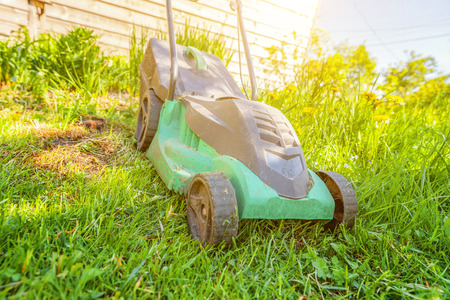 Lawn mower cutting green grass in backyard in sunny day. Gardening country lifestyle background. Beautiful view on fresh green grass lawn in sunlight, garden landscape in spring or summer seasonの写真素材