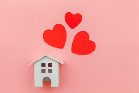 Simply minimal design with miniature white toy house with red heart isolated on pink pastel colorful trendy background. Mortgage property insurance dream home concept. Flat lay top view copy spaceの写真素材
