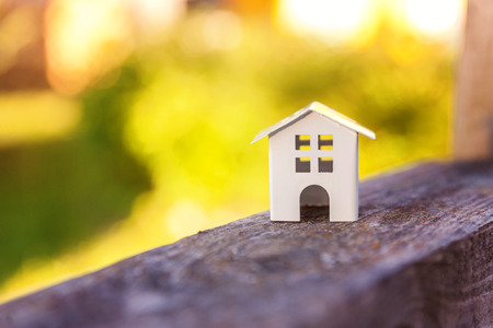 Miniature white toy model house in wooden background near green backdrop. Eco Village, abstract environmental background. Real estate mortgage property insurance dream home ecology conceptの写真素材