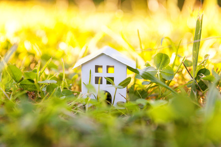 Miniature white toy model house in meadow with grass. Eco Village, abstract environmental background. Real estate mortgage property insurance dream home ecology conceptの写真素材